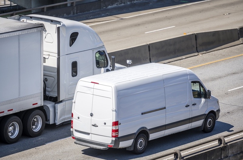 A White Freight Truck and White Delivery Van Driving Down the Highway A White Freight Truck and White Delivery Van Driving Down the Highway